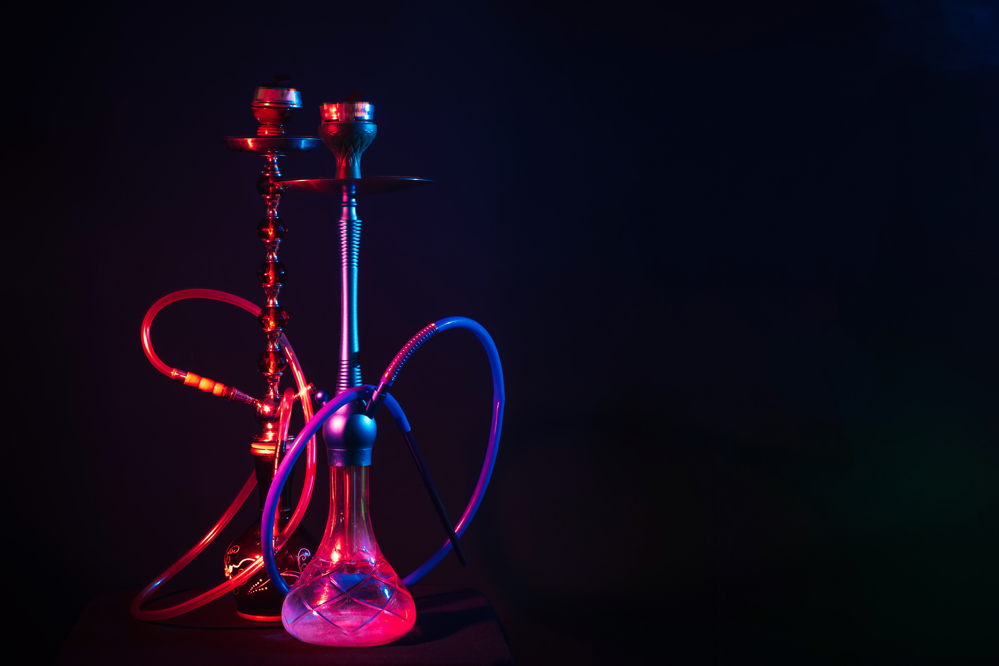 two hookahs with red and blue neon lighting on the table in the lounge cafe